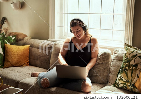 Computer, headphones and woman on sofa and music, happy work from home for mental health in apartment. Young person relax on couch and listening to audio technology, electronics and working on laptop 132006121