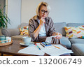 Middle aged woman reviewing expenses receipts while sitting on couch with coffee and phone in cozy living space. Managing personal finances with mobile app . Checking financial balance, budgeting. 132006749