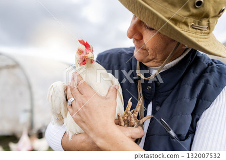 Farmer, woman and holding chicken for agriculture in field, environment and countryside. Poultry farming, female worker and feather birds for sustainability, eggs production and food trade industry Farmer, woman and holding chicken for agriculture in field, environment and countryside. Poultry farming, female worker and feather birds for sustainability, eggs production and food trade industry 132007532