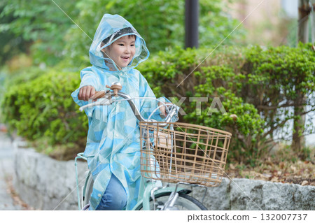 A child riding a bicycle in a raincoat on a rainy day A child riding a bicycle in a raincoat on a rainy day 132007737