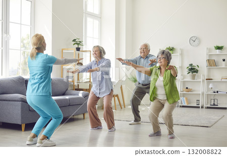 Young nurse squating with group of old men and women during physiotherapy. 132008822