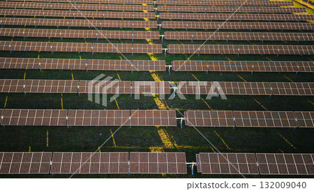 Drone view of a solar energy station with multiple rows of photovoltaic panels aligned in symmetry on green grass, generating renewable electricity. 132009040