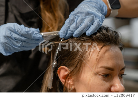 A stylist applies hair dye with precision while a client relaxes in the salon chair. The atmosphere is calm and professional. 132009417