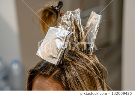 A client undergoing a hair coloring treatment with foils applied in a bright, modern salon environment during the day. 132009420