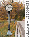 An attractive clock is positioned along a curving path in a park, framed by vibrant autumn leaves and nearby benches inviting relaxation. 132009453