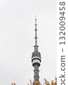 High above the city, a tall communication tower rises into the cloudy sky, showcasing modern engineering against the backdrop of overcast weather. 132009458