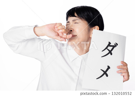 A senior woman holding a piece of paper with "no" written on it and pretending to resist 132010552