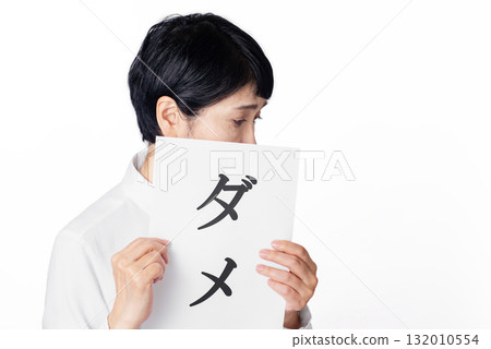 A senior woman wearing a white shirt with a sad expression holding a piece of paper that says "No" A senior woman wearing a white shirt with a sad expression holding a piece of paper that says "No" 132010554
