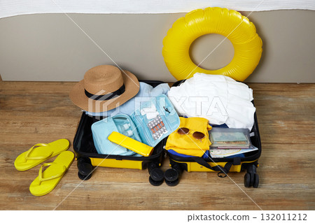Colorful summer essentials including a sun hat, sandals, and a swim ring are neatly packed in a suitcase 132011212