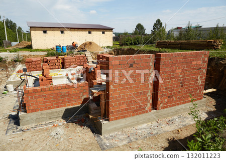 Brick walls are rising at a construction site, supported by wooden forms and metal rods. Brick walls are rising at a construction site, supported by wooden forms and metal rods. 132011223
