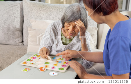 Nurse in nursing home helping a senior woman with number puzzle.  . Dementia, Alzheimer's disease concept 132011356