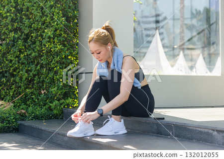 Active woman sport workout fit people stretch muscles outdoors preparing for exercise tying running shoes on steps wearing smartwatch earbuds ready for invigorating fitness stretch healthy lifestyle. 132012055
