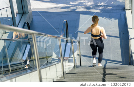Fit woman performs sport exercise workout, ascending concrete steps in a bright urban outdoor environment, demonstrating dedication to a healthy fit body, encouraging active lifestyle. Fit woman performs sport exercise workout, ascending concrete steps in a bright urban outdoor environment, demonstrating dedication to a healthy fit body, encouraging active lifestyle. 132012073