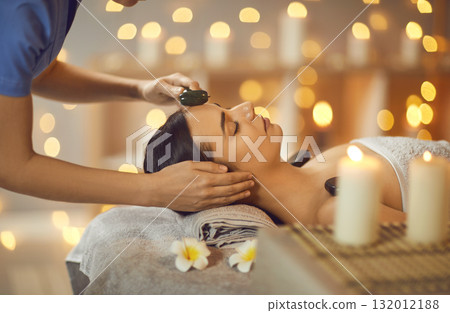 Relaxed young woman is getting beauty face massage with facial roller at spa salon Relaxed young woman is getting beauty face massage with facial roller at spa salon 132012188