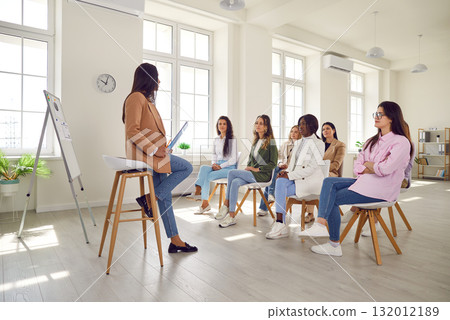 Young woman coach gives presentation for diverse women at professional business training meeting Young woman coach gives presentation for diverse women at professional business training meeting 132012189