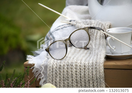 Cozy scene featuring glasses, a knitted scarf, and a cup of tea, perfect for relaxation. Cozy scene featuring glasses, a knitted scarf, and a cup of tea, perfect for relaxation. 132013075