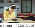 Happy young Asian student wearing headphones and using a tablet, enjoying online lessons, studying in the library. 132013116