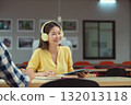 Happy young Asian student wearing headphones and using a tablet, enjoying online lessons, studying in the library. 132013118