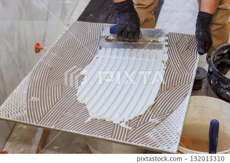 Worker uses trowel to spread adhesive on large tile ready for installation at building site. Worker uses trowel to spread adhesive on large tile ready for installation at building site. 132013310
