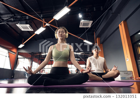 Young man and woman sitting on the floor on mats and practicing yoga in the lotus pose with their eyes closed. 132013351