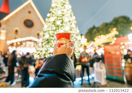 Woman hand holding glasses mugs with Germany red mulled wine on Christmas Market. The winter drink Traditional alcoholic drinks on German xmas funfair. Merry Christmas and happy New Year concept 132013422