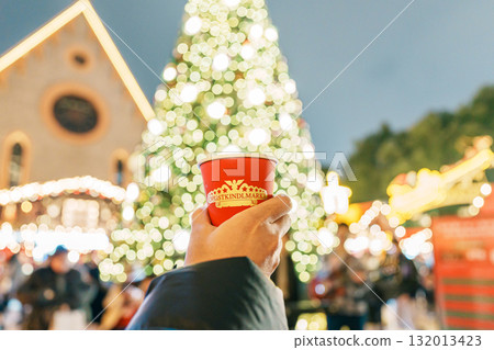 Woman hand holding glasses mugs with Germany red mulled wine on Christmas Market. The winter drink Traditional alcoholic drinks on German xmas funfair. Merry Christmas and happy New Year concept 132013423