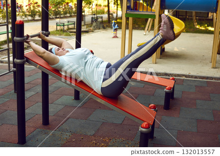 Overweight woman doing physical exercises on training equipment at sports ground 132013557