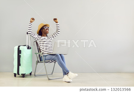 African American woman with suitcase and laptop gets happy when she books cheap holiday tickets 132013566