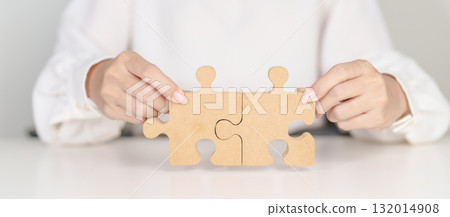 Woman connecting couple puzzle piece, wood jigsaw on table. Business solutions, mission, success, goals, strategy, Teamwork, Idea, Solution and challenge concepts 132014908