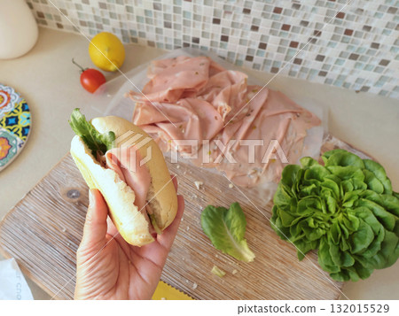Anonymous person makes sandwich with sausage, lettuce, and mortadella, homemade mayonnaise in kitchen. Italian cuisine, high-quality farm-grown ingredients. Anonymous person makes sandwich with sausage, lettuce, and mortadella, homemade mayonnaise in kitchen. Italian cuisine, high-quality farm-grown ingredients. 132015529