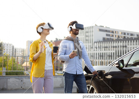 A couple wearing VR headsets while an electric vehicle charges, suggesting a futuristic experience. 132015653