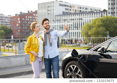 A smiling couple takes a selfie while their electric vehicle charges in an urban setting, highlighting modern eco-friendly transportation. A smiling couple takes a selfie while their electric vehicle charges in an urban setting, highlighting modern eco-friendly transportation. 132015675