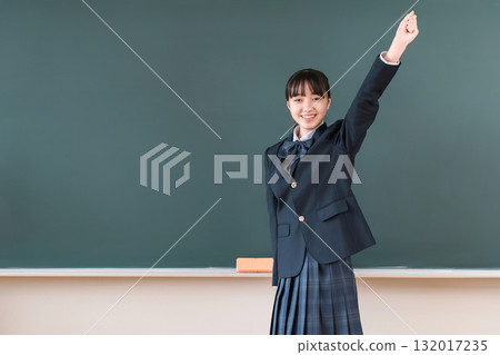 Female elementary, junior high, and high school students in blazers standing in front of the blackboard and making a fist pump 132017235