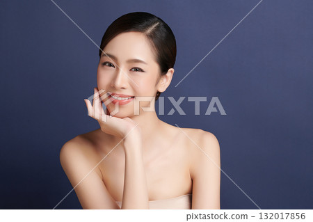 A beautiful young Asian woman with clean, fresh skin against a blue background. Skincare, facial treatment, cosmetology, beauty, and spa. An elegant portrait of an Asian woman. A beautiful young Asian woman with clean, fresh skin against a blue background. Skincare, facial treatment, cosmetology, beauty, and spa. An elegant portrait of an Asian woman. 132017856