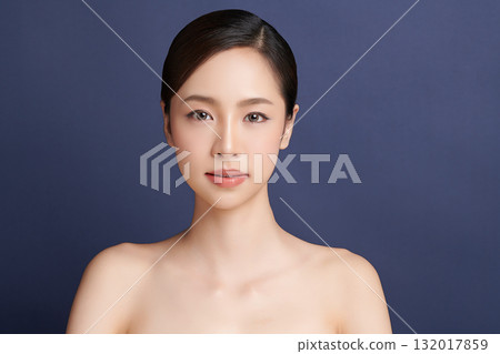 A beautiful young Asian woman with clean, fresh skin against a blue background. Skincare, facial treatment, cosmetology, beauty, and spa. An elegant portrait of an Asian woman. 132017859