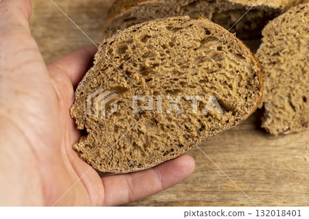 a sliced loaf of rye flour bread lies on the table on a cutting board, a small elongated loaf of freshly baked rye bread on an old cutting board while slicing bread a sliced loaf of rye flour bread lies on the table on a cutting board, a small elongated loaf of freshly baked rye bread on an old cutting board while slicing bread 132018401