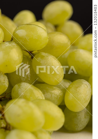 a branch of ripe beautiful green grapes lying on the table, covered with drops of water, wet fruits of pure green grapes on a branch a branch of ripe beautiful green grapes lying on the table, covered with drops of water, wet fruits of pure green grapes on a branch 132018403