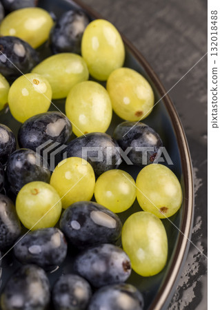 wet beautiful ripe grapes of blue and green color lying on a bowl, covered with drops of water, wet fruits of pure green and blue grapes during cooking 132018488