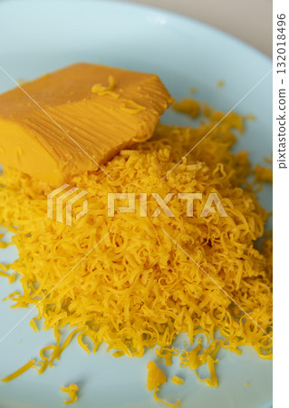a piece of whole cheese and a large amount of finely grated yellow cheese made from fresh milk, grating fresh orange cheese for pizza or pasta 132018496