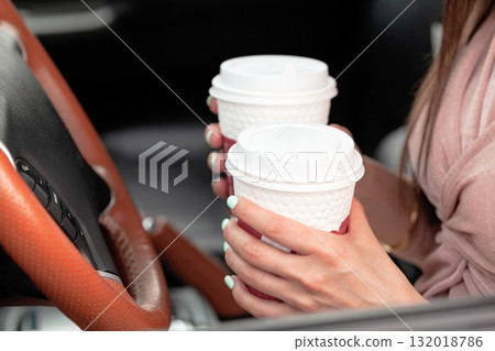 Closeup shot of hands of female driver who holds two paper cups with tea or coffee Closeup shot of hands of female driver who holds two paper cups with tea or coffee 132018786