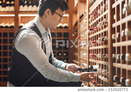 Professional Sommelier Selecting Fine Wine Bottle in Traditional Wooden Cellar 132020773