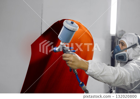 Car spray painter sprays red paint to the part of vehicle from spray gun in industrial chamber, close up. Car spray painter sprays red paint to the part of vehicle from spray gun in industrial chamber, close up. 132020800
