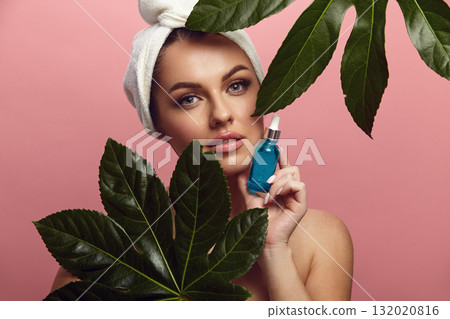 Woman holds facial serum among tropical leaves on a pink isolated. Woman holds facial serum among tropical leaves on a pink isolated. 132020816