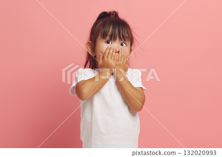 Shocked little girl covers mouth with hands stares scared at camera cannot believe in something horrible dressed in white t shirt isolated over pink background. Shocked little girl covers mouth with hands stares scared at camera cannot believe in something horrible dressed in white t shirt isolated over pink background. 132020993