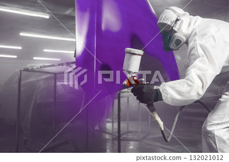 Car repair painter in protective overalls and painting a respirator part of car in the paint chamber 132021012