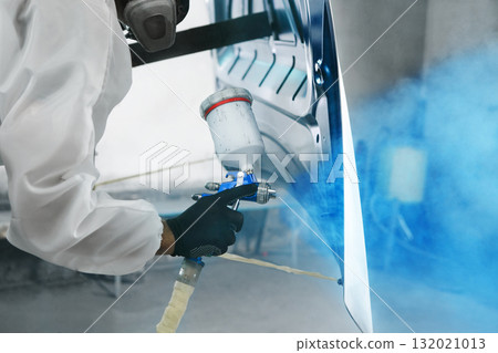 Professional male car painter sprays paints car part to blue color in garage by airbrush. Man works with spray gun. Professional male car painter sprays paints car part to blue color in garage by airbrush. Man works with spray gun. 132021013