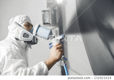 Close up shot of automobile repairman painter in mask and protective workwear painting part of car in paint chamber. Close up shot of automobile repairman painter in mask and protective workwear painting part of car in paint chamber. 132021014