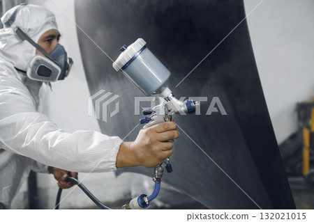 Spray painter worker in protective glove with airbrush pulverizer varnishing and painting car body in paint chamber. 132021015