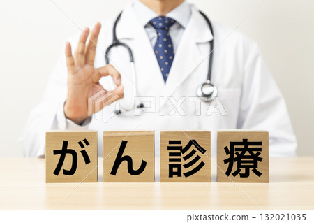 A block with the words "Cancer Treatment" written on it and a doctor making an OK sign 132021035
