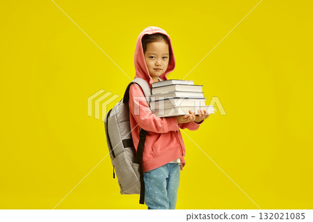 Lovely smiling little girl in casual clothing with a backpack and books posing over yellow isolated background. First time to school. Lovely smiling little girl in casual clothing with a backpack and books posing over yellow isolated background. First time to school. 132021085